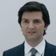 Adam Scott, in an blue-gray business suit, has the world's most awkward smile.